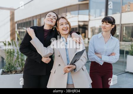 Tre donne professionisti che condividono un momento all'aperto vicino a un moderno edificio per uffici Foto Stock