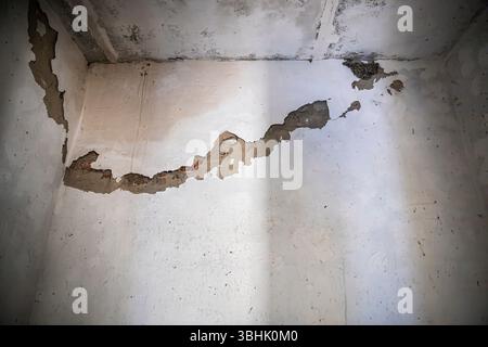 Primo piano di una vecchia parete in gesso bianco con grandi crepe e aree di sbucciatura che espongono mattoni rossi sotto. Ideale per temi di rinnovamento, decadenza, costr Foto Stock