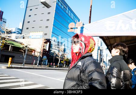 Un giovane uomo con una felpa con cappuccio e un soffione North Face attende fuori dal mercato di Tsukiji Foto Stock