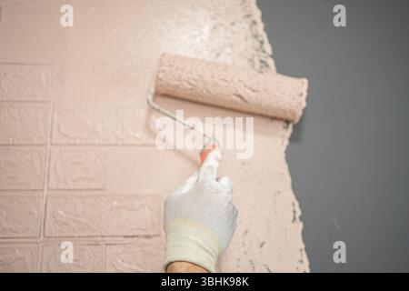 Persona che dipinge un muro in mattoni con un rullo di pittura Foto Stock