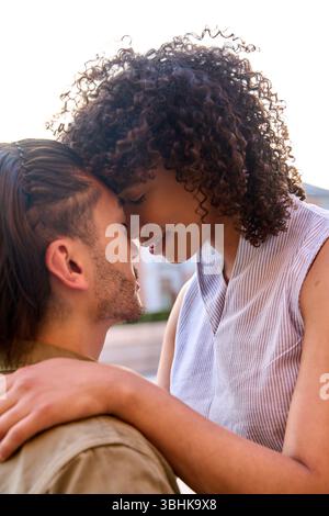 Coppia romantica che tocca la fronte, assaporando un momento tenero all'aperto, irradiando amore e intimità sotto la calda luce del sole estivo Foto Stock