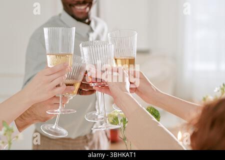 Gruppo di giovani adulti e persone di mezza età che si brunano durante la celebrazione del matrimonio, mani visibili che tengono vino e bicchieri da champagne durante il brindisi festivo Foto Stock
