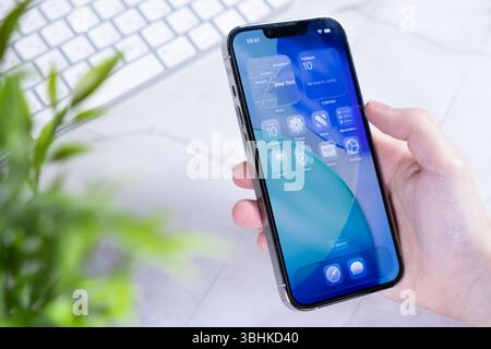 Poznan, Polonia - 10 giugno 2025: Mano che tiene in mano uno smartphone moderno che visualizza il nuovo sistema operativo iOS 26 con innovativo design dello schermo in vetro liquido Foto Stock