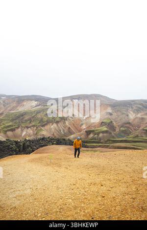 Hiker walks along sand and stone path through the colorful rhyolite mountains of Landmannalaugar in Icelands Highlands, a peaceful journey into wild v Foto Stock