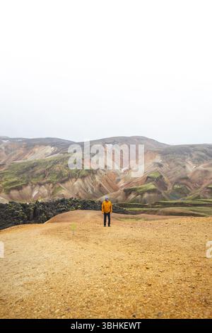 Hiker walks along sand and stone path through the colorful rhyolite mountains of Landmannalaugar in Icelands Highlands, a peaceful journey into wild v Foto Stock