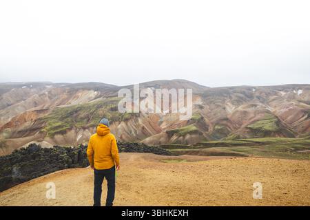 Hiker walks along sand and stone path through the colorful rhyolite mountains of Landmannalaugar in Icelands Highlands, a peaceful journey into wild v Foto Stock