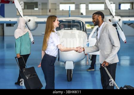 Pilota donna che stringe la mano a un uomo d'affari all'interno di un hangar aereo, salutando un passeggero prima di un volo privato Foto Stock