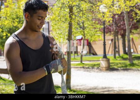 Latino pugile atleta uomo mettendo guanti pronti per allenarsi all'aperto Foto Stock