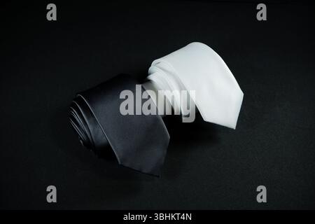 cravatte in bianco e nero isolate su sfondo nero, cravatte alla moda maschile in bianco e nero arrotolate con vista ad alto angolo Foto Stock