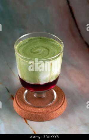 Un latte matcha di fragole a strati in un bicchiere, che mostra la vivace base di fragole rosse e il top matcha verde Foto Stock