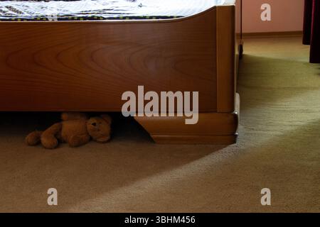 Orsacchiotto giace sul pavimento sotto un letto di legno nella camera da letto, un giocattolo per bambini su un tappeto, interno della stanza Foto Stock