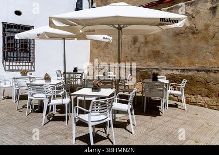 Cordova, Cordova - Spagna - 04-08-2024: Un caffè all'aperto con tavoli coperti da ombrello bianco, adagiato su una storica parete di pietra a Cordova. Foto Stock