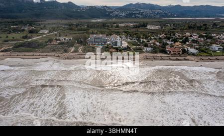 Denia, Alicante - Spagna - 11-13-2024: Vista aerea di una costa turbolenta con grandi onde che si infrangono sulla spiaggia, con una zona residenziale. Foto Stock