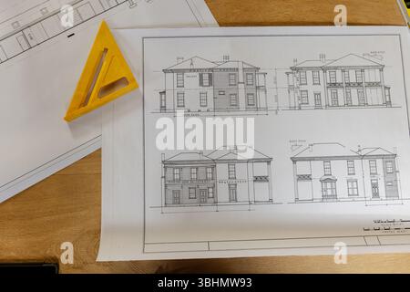 Piano di elevazione della casa adagiato su una scrivania in legno in ufficio, con righello triangolare giallo Foto Stock