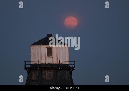 Dovercourt Essex, Regno Unito. 10 giugno 2025. La Full Strawberry Moon sorge sul faro inferiore di Dovercourt, Essex, Regno Unito. La Luna piena si trova in basso sull'orizzonte meridionale, dando l'illusione di una Luna sovradimensionata causata da ciò che è noto come un grave stallo lunare che si verifica ogni 18,6 anni. Crediti: MARTIN DALTON/Alamy Live News Foto Stock