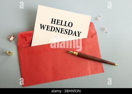 Su un tavolo di legno chiaro, c'è un ramo di eucalipto, una penna stilografica e un foglio di carta con il testo HELLO WEDNESDAY Foto Stock