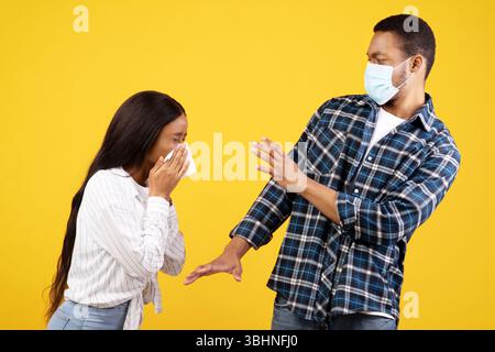 Giovane donna afroamericana che soffia il naso, il tipo spaventato in maschera protettiva tira via durante la quarantena Foto Stock