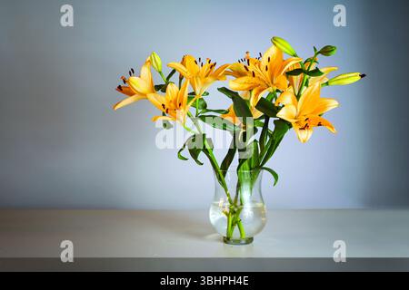 Bouquet di fiori con gigli arancioni in un vaso di vetro su un tavolo di fronte a sfondo grigio blu con spazio di copia, messa a fuoco selezionata Foto Stock