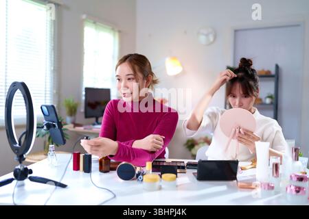 Due giovani donne asiatiche che creano contenuti di bellezza con cosmetici e illuminano anulare in casa studio. Tutorial online sul trucco video in live streaming per i farmaci social Foto Stock