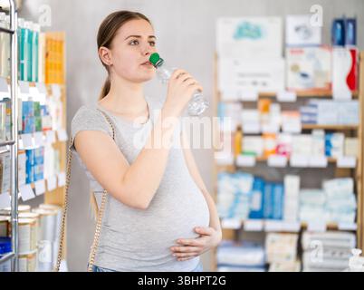 La ragazza incinta in farmacia beve l'acqua dalla bottiglia Foto Stock