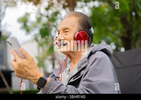 Visione laterale del ritratto di un anziano che indossa le cuffie e si diverte all'aperto, magari ascoltando musica o guardando un video. Foto Stock