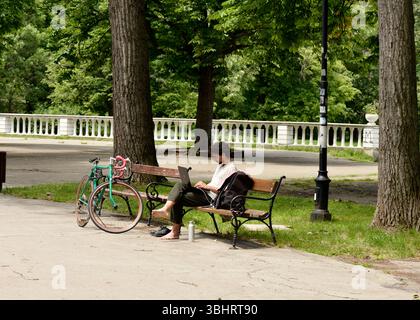 Un giovane a piedi nudi lavora con il proprio laptop in un parco cittadino, ibrido flessibile e lavoro a distanza da casa Foto Stock