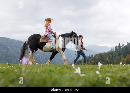 Ragazza in un'avventura a cavallo tra le montagne nebbiose, lezione di equitazione nella natura panoramica presso la scuola di equitazione con istruttore cowgirl esperto Foto Stock