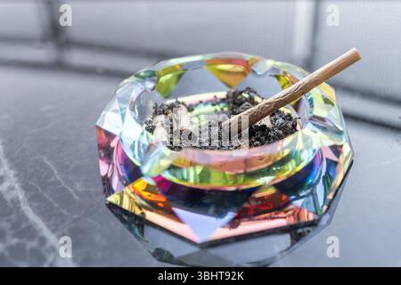 Posacenere luminoso con articolazioni di cannabis e cenere su un tavolo in marmo riflettente, catturato in un ambiente tranquillo per evocare relax, stile di vita e cultura contemporanea. Foto Stock