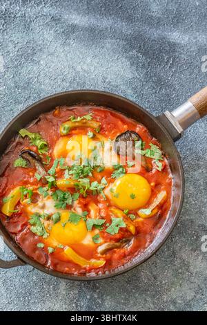 Uova sospese a base di pomodoro speziato con funghi, peperoni ed erbe fresche Foto Stock