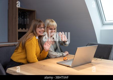 Due donne d'affari professionali nell'ufficio dell'azienda vinicola che collaborano alla strategia di marketing, incentrata sullo schermo di un notebook, circondate da energia positiva, branding Foto Stock