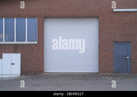 Borken, NRW, Germania, porta a serranda bianca chiusa e porta laterale blu su una parete di mattoni rossi di un edificio industriale, Europa Foto Stock