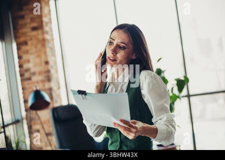 Donna d'affari professionale in un ufficio moderno che parla al telefono e rivede documenti Foto Stock
