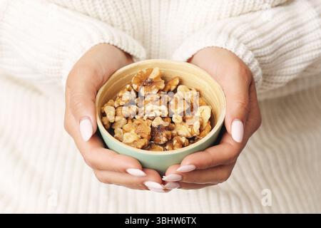 Noci biologiche in un recipiente piccolo. Mani che tengono con cura cibo sano per il cervello. Snack naturali e salutari. Primo piano con toni luminosi Foto Stock