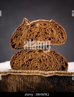 Due metà di pane a lievitazione naturale di segale a sezione su una tavola rustica di legno. Pagnotta artigianale in stile fattoria catturata dalla calda luce naturale Foto Stock