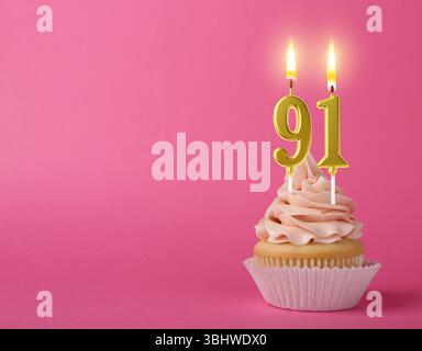 Delizioso cupcake con candele a forma di numero su sfondo rosa, spazio per il testo. 91° compleanno o altra occasione speciale Foto Stock