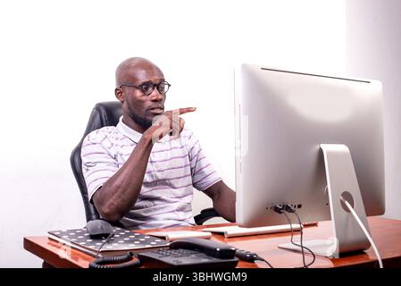 giovane uomo d'affari seduto alla scrivania, che lavora e punta il dito sullo schermo del notebook Foto Stock