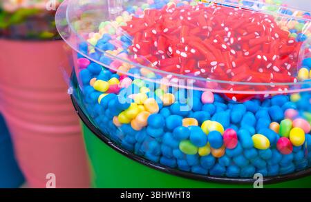 Vivace assortimento di gelatine multicolore e bastoncini di liquirizia rossi esposti in un cestino trasparente. Perfetto per il negozio di dolci, eventi per bambini Foto Stock