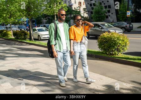 Amanti felici coppia di studenti afroamericani che camminano insieme, si tengono per mano, ridono allegramente. Foto Stock