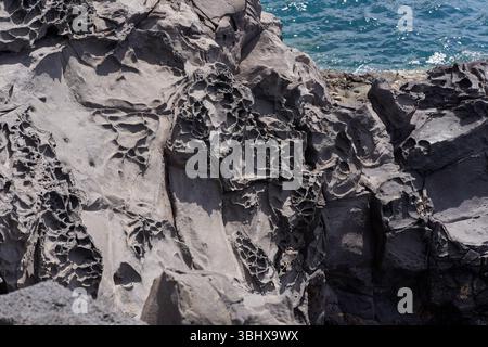 Primo piano di rocce vulcaniche intemprate con buchi erosi vicino all'oceano a Playa de Montaña Amarilla a Tenerife Foto Stock