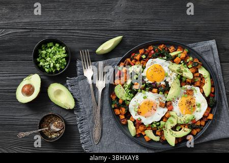 Cubetti di patate dolci fritti e serviti con uova con il lato soleggiato e fette di avocado fresche su un piatto piatto piatto nero, non generati dall'IA Foto Stock