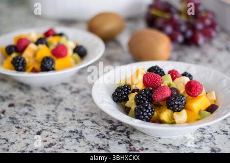 Ciotola con frutta fresca tagliata e frutti di bosco sul bancone della cucina Foto Stock