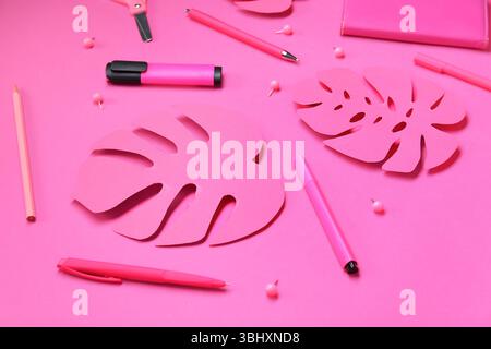 Composizione con diversi tipi di cartoleria e foglie di palma di carta su sfondo rosa Foto Stock