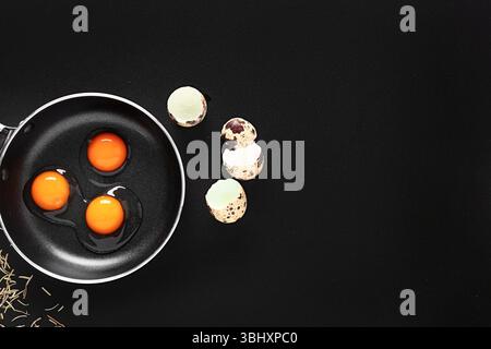 Gusci d'uovo e padella con uova di quaglia crude su sfondo nero Foto Stock