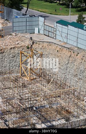 Una gru da cantiere solleva un'ulteriore sezione di gru su un gancio per aumentare l'altezza. Cantiere, pozzo di fondazione. Foto Stock