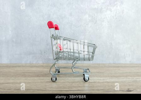 Carrello della spesa in miniatura su una superficie in legno con sfondo grigio Foto Stock