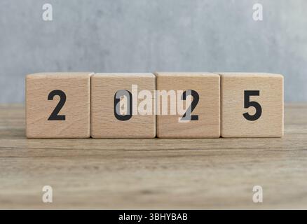 Blocchi in legno che espongono l'anno 2025 su una superficie in legno con sfondo grigio Foto Stock