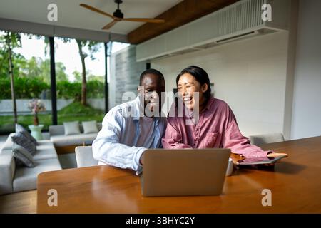 Felice coppia multietnica che utilizza un notebook, acquista online con le vendite, gioca insieme Foto Stock