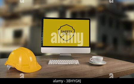 Una postazione di lavoro per la sicurezza sul luogo di lavoro in cantiere con casco di sicurezza, monitor per computer che visualizza messaggi di sicurezza e tazza da caffè, sottolineando l'importanza Foto Stock