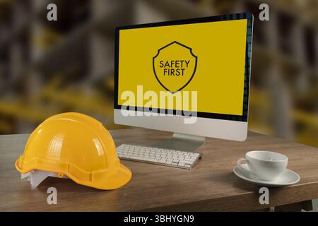 Una postazione di lavoro per la sicurezza sul luogo di lavoro in cantiere con casco di sicurezza, monitor per computer che visualizza messaggi di sicurezza e tazza da caffè, sottolineando l'importanza Foto Stock