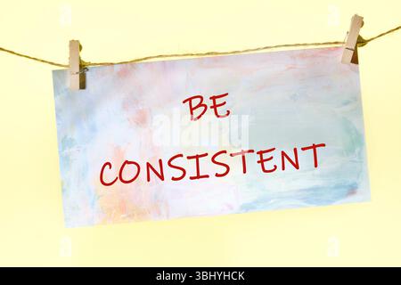 Il testo del concetto aziendale DEVE ESSERE COERENTE scritto su un cartello colorato su una corda con clothespin. Foto Stock